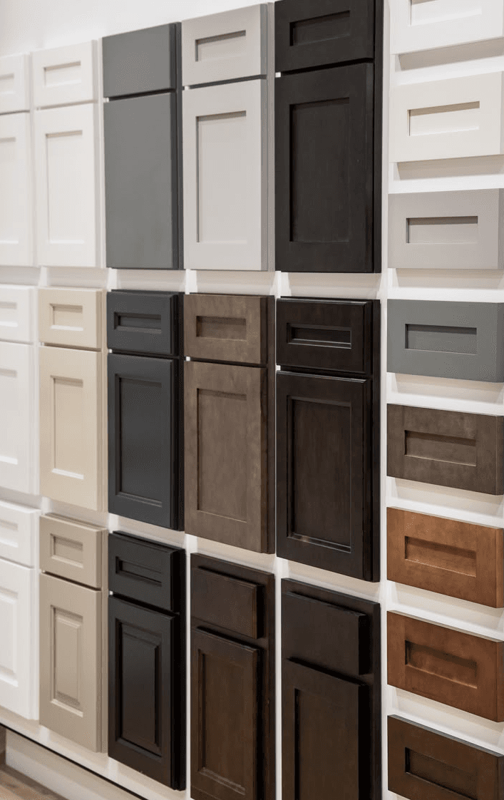 A wall display of cabinet door samples — white shaker, dark grey, walnut, painted finishes — for the customer to handle and compare